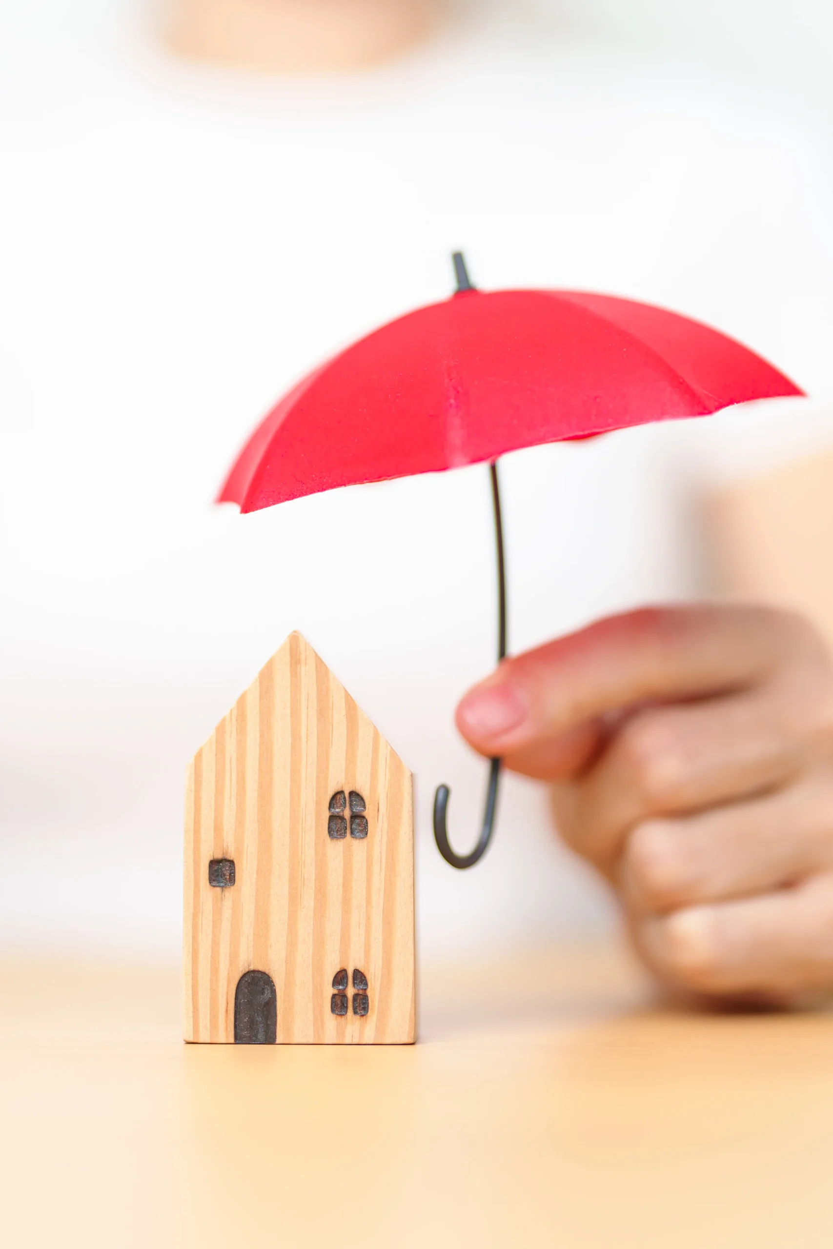 Businesswoman hand holding red Umbrella cover wooden Home model. real estate, insurance and property concepts